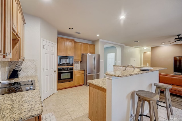 kitchen with a breakfast bar, arched walkways, decorative backsplash, visible vents, and black appliances