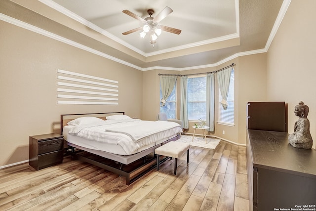 bedroom featuring baseboards, a raised ceiling, light wood-style flooring, and ornamental molding