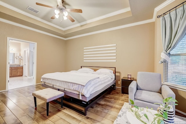 bedroom featuring visible vents, wood finished floors, connected bathroom, ornamental molding, and a tray ceiling