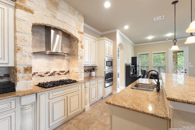 kitchen with wall chimney range hood, stainless steel appliances, decorative backsplash, and a sink