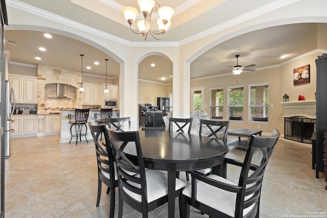 dining space with crown molding, arched walkways, a fireplace, ceiling fan with notable chandelier, and recessed lighting