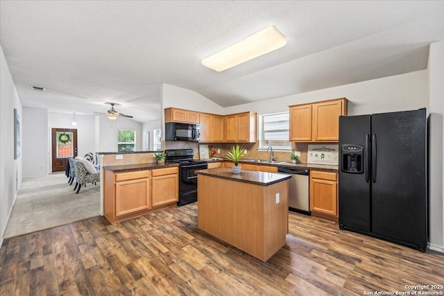 kitchen featuring dark countertops, a center island, a sink, black appliances, and lofted ceiling