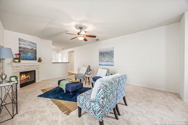 carpeted living room with baseboards, ceiling fan, a lit fireplace, and visible vents