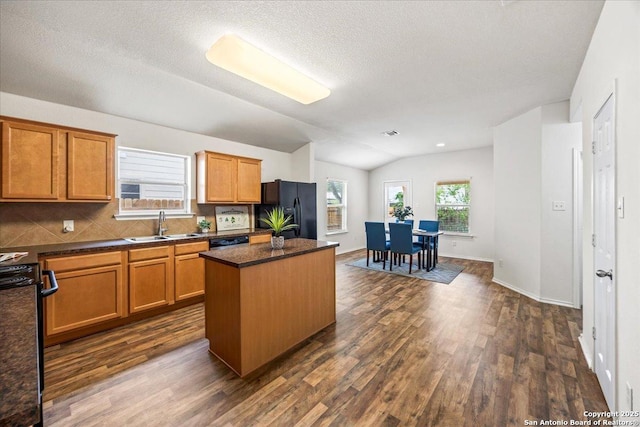 kitchen with dark wood-style flooring, a kitchen island, dark countertops, a sink, and black appliances