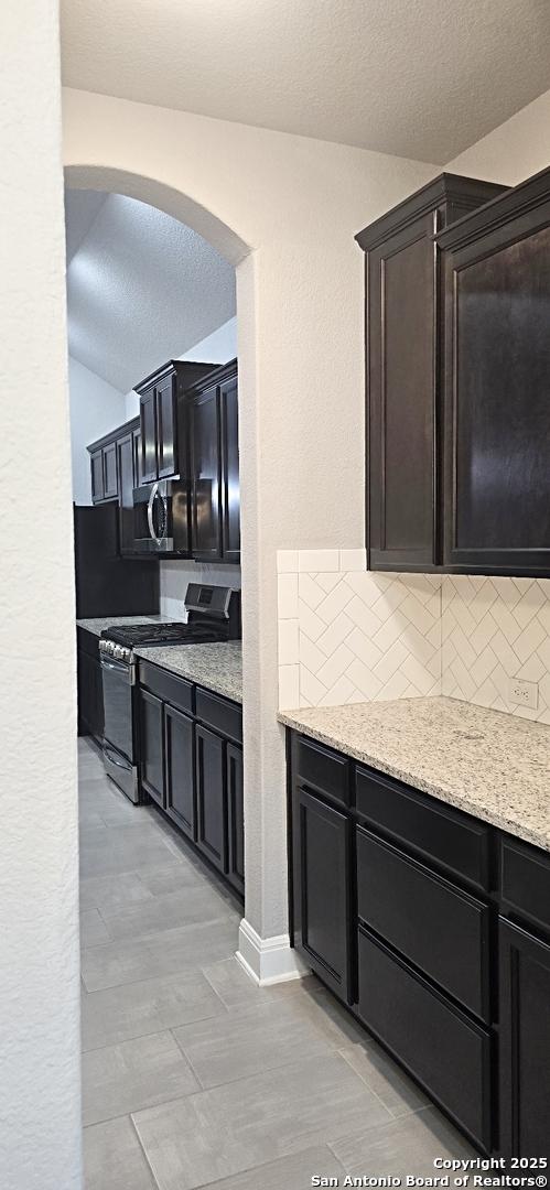 kitchen featuring stainless steel gas range, arched walkways, light stone countertops, and tasteful backsplash