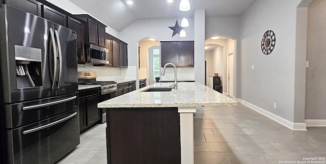 kitchen featuring light stone countertops, arched walkways, tasteful backsplash, a sink, and appliances with stainless steel finishes