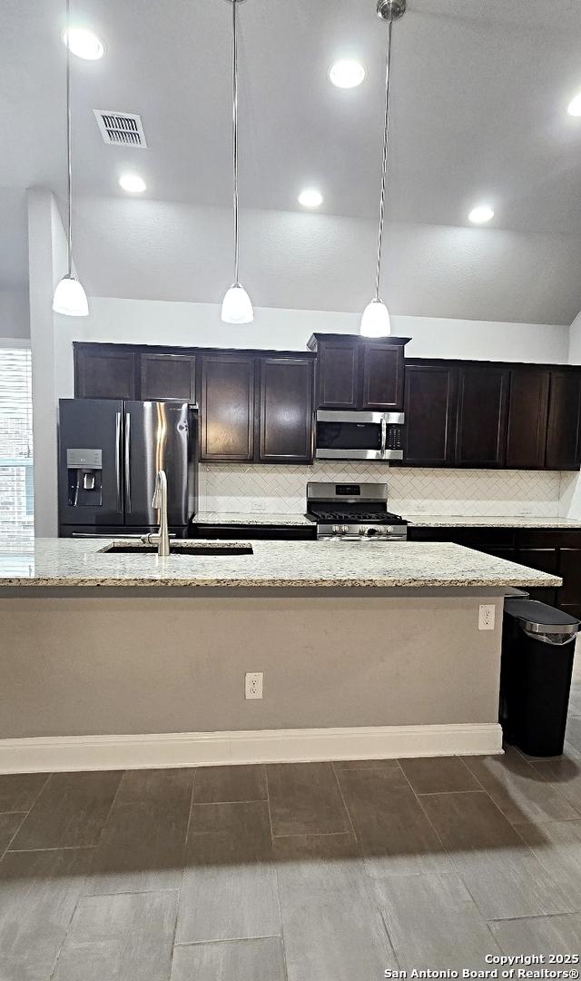 kitchen featuring tasteful backsplash, light stone countertops, stainless steel appliances, and decorative light fixtures