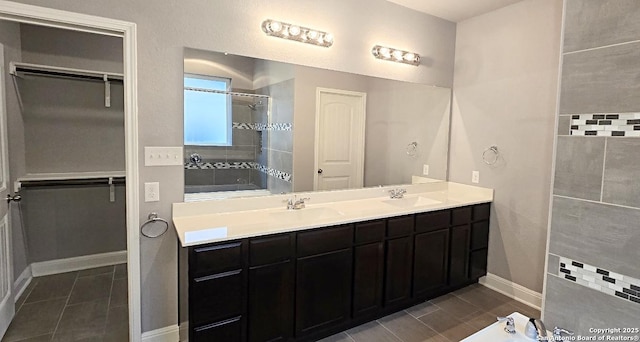 full bathroom with double vanity, tile patterned flooring, a tile shower, a sink, and baseboards
