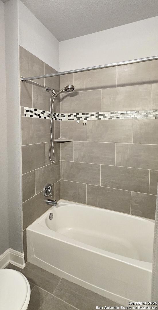 bathroom featuring shower / bathtub combination, toilet, tile patterned flooring, and a textured ceiling