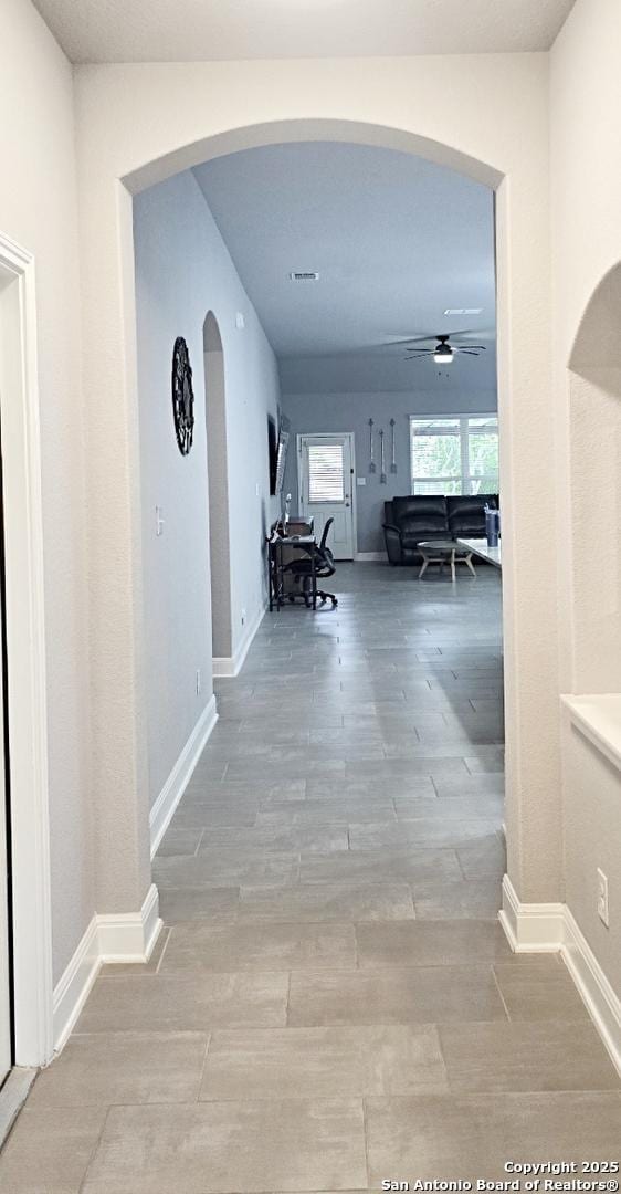 hall featuring arched walkways, baseboards, and wood finished floors