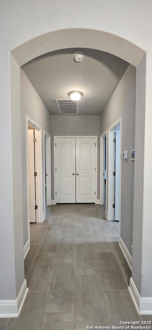 hall featuring baseboards, tile patterned flooring, arched walkways, and visible vents