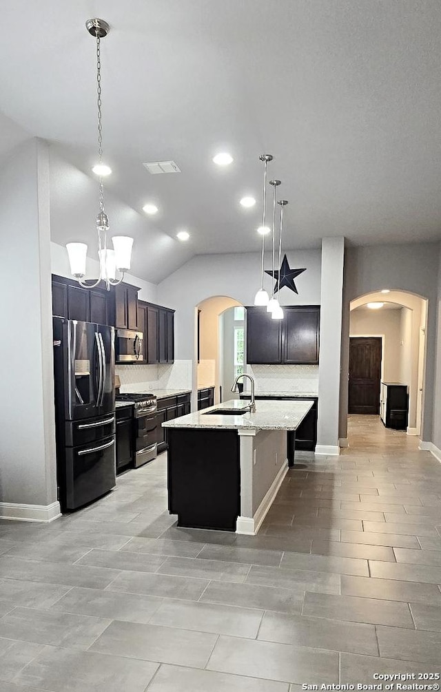 kitchen with decorative backsplash, a kitchen island with sink, arched walkways, a sink, and stainless steel appliances