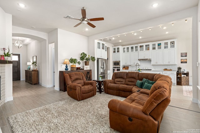 living room featuring arched walkways, ceiling fan, baseboards, and light wood-style flooring