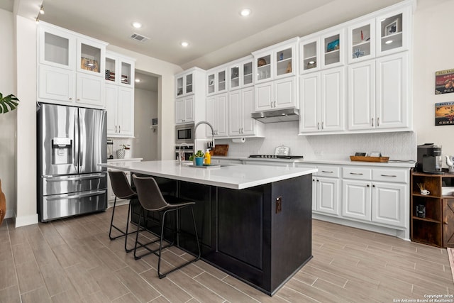 kitchen featuring light wood-style flooring, stainless steel appliances, backsplash, visible vents, and a center island with sink