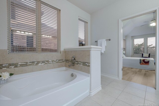 bathroom with tile patterned floors, ceiling fan, baseboards, and a bath