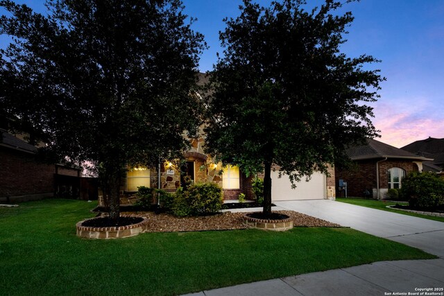 view of property hidden behind natural elements with concrete driveway, a lawn, an attached garage, and brick siding