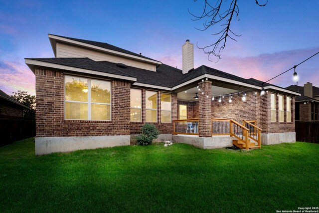 back of house at dusk featuring brick siding, ceiling fan, a yard, and a chimney