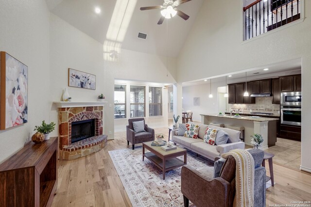 living area featuring high vaulted ceiling, a ceiling fan, light wood-style flooring, and visible vents