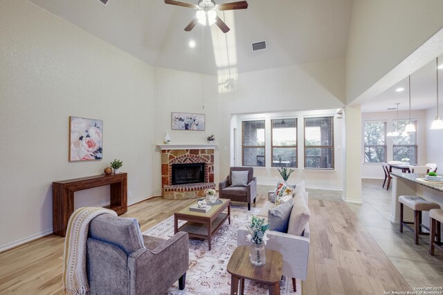 living room featuring light wood finished floors, high vaulted ceiling, a ceiling fan, baseboards, and visible vents