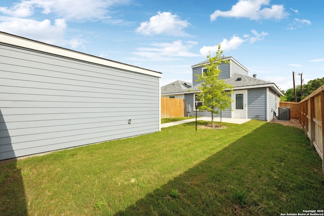 rear view of property with a yard, a shingled roof, central AC unit, and a fenced backyard