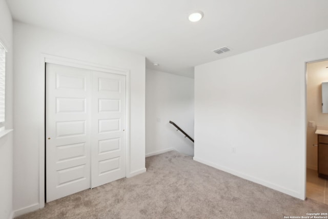 unfurnished bedroom featuring visible vents, baseboards, a closet, ensuite bathroom, and light carpet