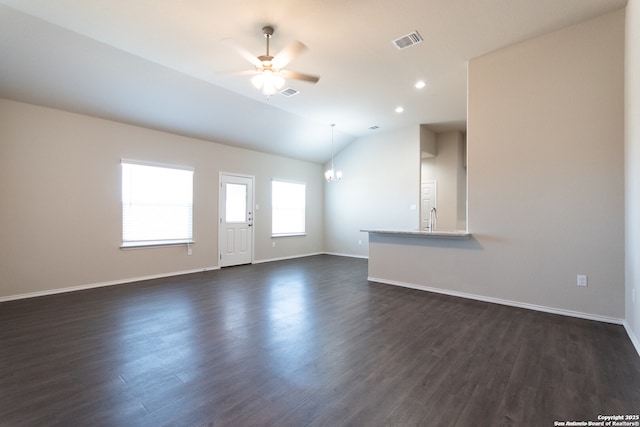 unfurnished living room with visible vents, dark wood finished floors, ceiling fan with notable chandelier, baseboards, and vaulted ceiling
