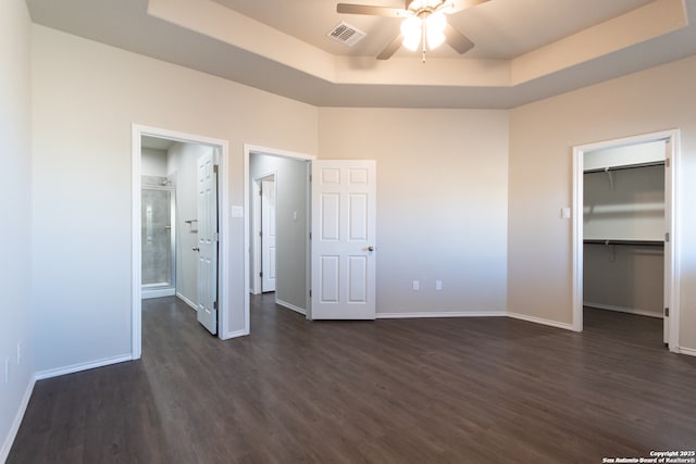 unfurnished bedroom featuring visible vents, a raised ceiling, baseboards, a spacious closet, and dark wood-type flooring