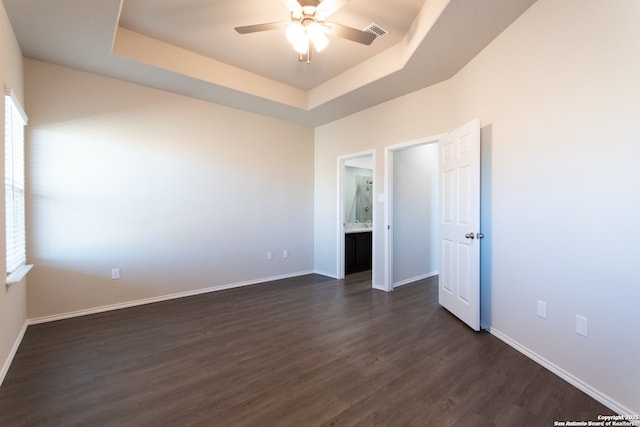 unfurnished room featuring visible vents, dark wood-style flooring, baseboards, ceiling fan, and a tray ceiling