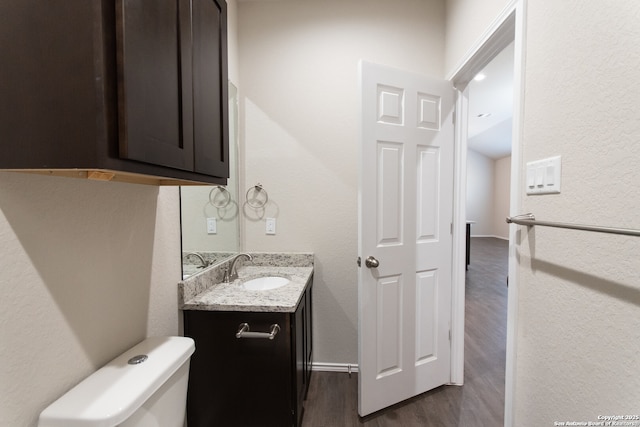 half bath with a textured wall, vanity, toilet, baseboards, and wood finished floors