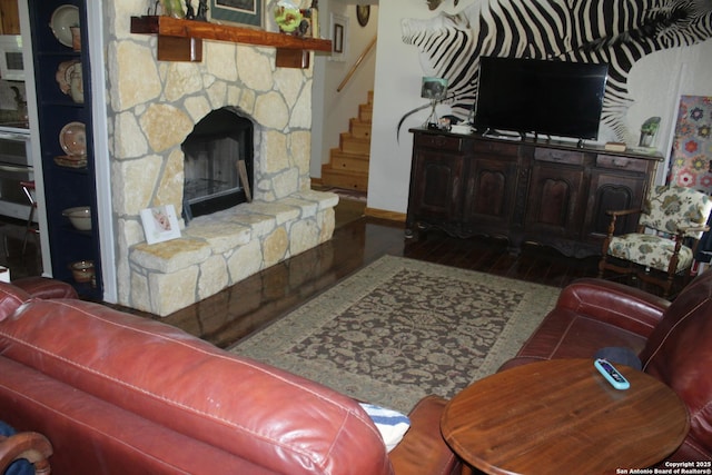 living area with stairs, baseboards, a stone fireplace, and wood finished floors
