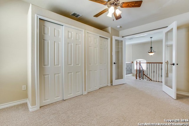 unfurnished bedroom featuring french doors, carpet flooring, two closets, and visible vents