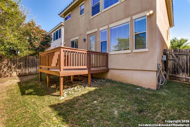rear view of house with a fenced backyard, a wooden deck, stucco siding, and a yard