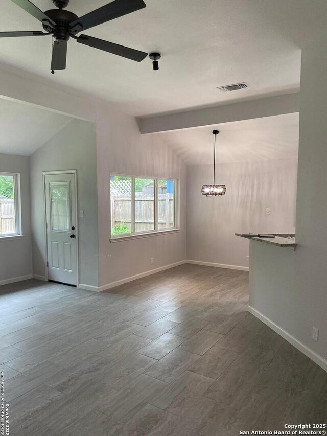 unfurnished living room featuring vaulted ceiling with beams, baseboards, ceiling fan with notable chandelier, and visible vents