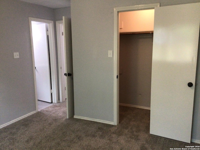 unfurnished bedroom with carpet flooring, baseboards, a walk in closet, and a closet