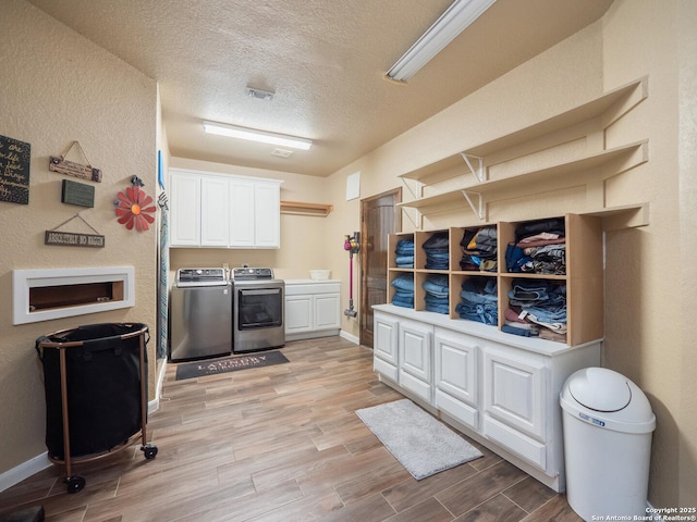 interior space featuring a textured ceiling, washing machine and clothes dryer, cabinet space, baseboards, and light wood finished floors