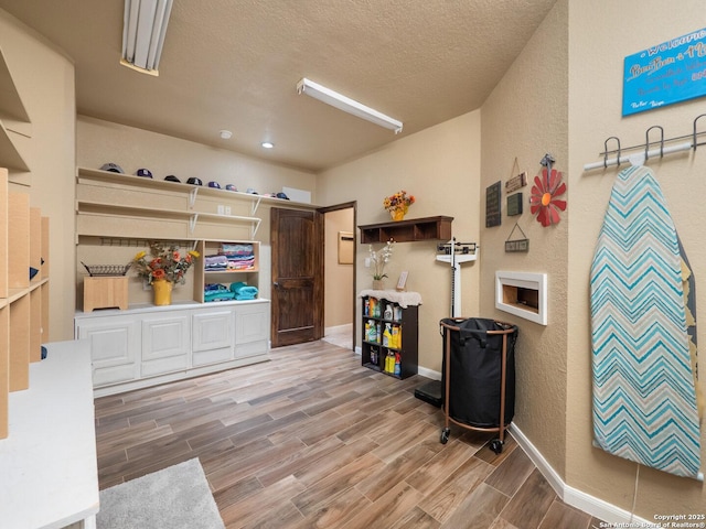 miscellaneous room with a textured ceiling, a textured wall, baseboards, and wood finished floors