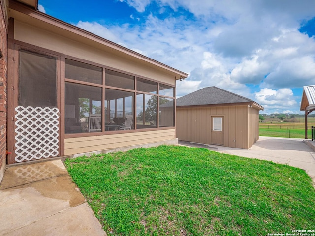 view of side of property featuring a lawn, fence, an outbuilding, and a sunroom
