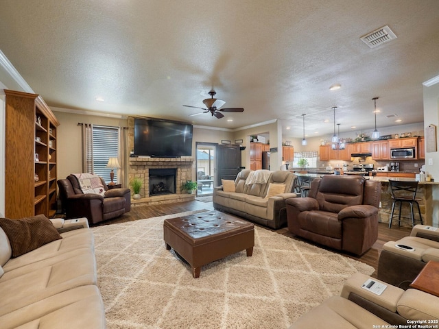 living area featuring a healthy amount of sunlight, ceiling fan, visible vents, crown molding, and wood finished floors