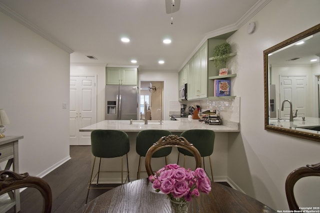 kitchen with crown molding, appliances with stainless steel finishes, a peninsula, decorative backsplash, and green cabinets