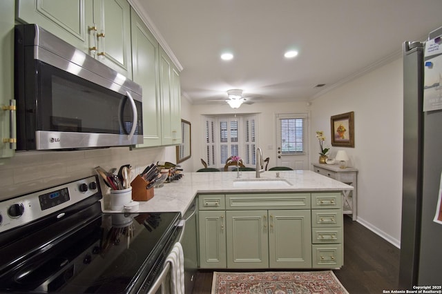 kitchen featuring crown molding, a peninsula, green cabinetry, a sink, and stainless steel appliances