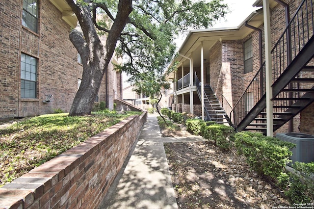 view of side of property featuring stairs, central AC, and brick siding