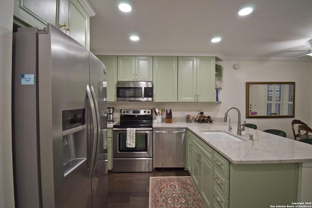 kitchen featuring dark wood-style flooring, a peninsula, green cabinetry, a sink, and appliances with stainless steel finishes