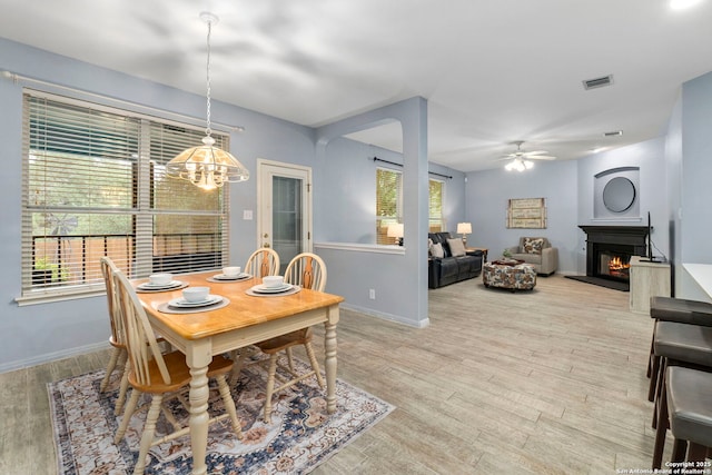 dining space featuring plenty of natural light, ceiling fan with notable chandelier, visible vents, and a lit fireplace
