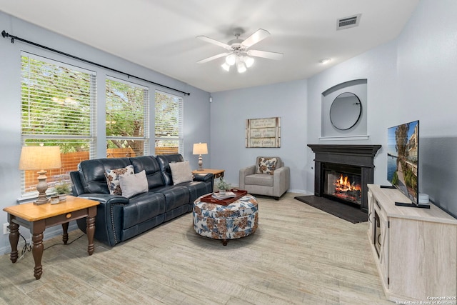 living room featuring a glass covered fireplace, ceiling fan, light wood-type flooring, and visible vents