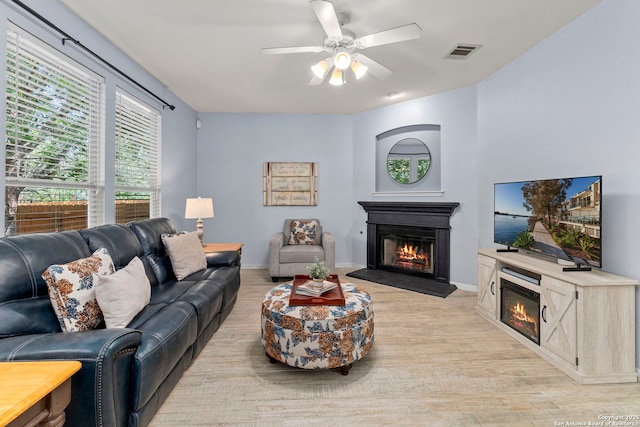 living area with visible vents, a glass covered fireplace, baseboards, ceiling fan, and light wood-type flooring