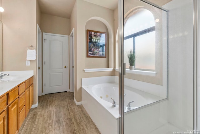 bathroom featuring a whirlpool tub, baseboards, wood finished floors, and vanity