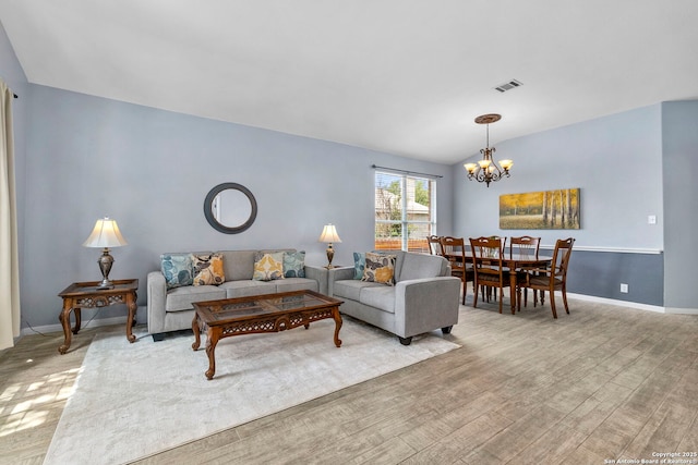living area featuring visible vents, lofted ceiling, wood finished floors, baseboards, and a chandelier