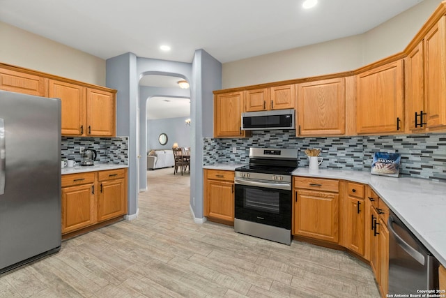 kitchen featuring light countertops, appliances with stainless steel finishes, backsplash, and arched walkways