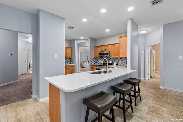 kitchen with a sink, stainless steel microwave, a breakfast bar area, and visible vents