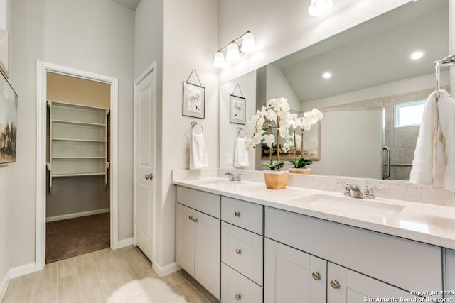 full bath featuring double vanity, a spacious closet, a sink, and a stall shower
